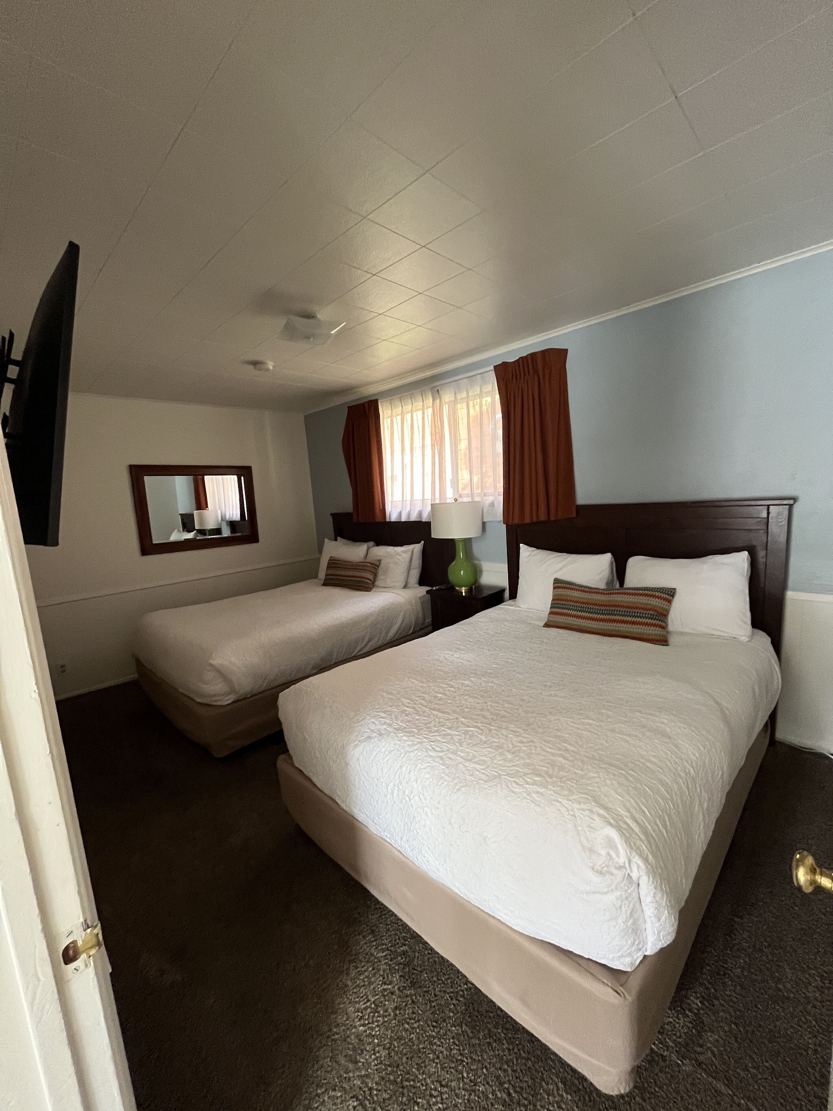 Een hotelkamer met twee bedden, een grote spiegel, een raam met gordijnen en een vloerbedekking.