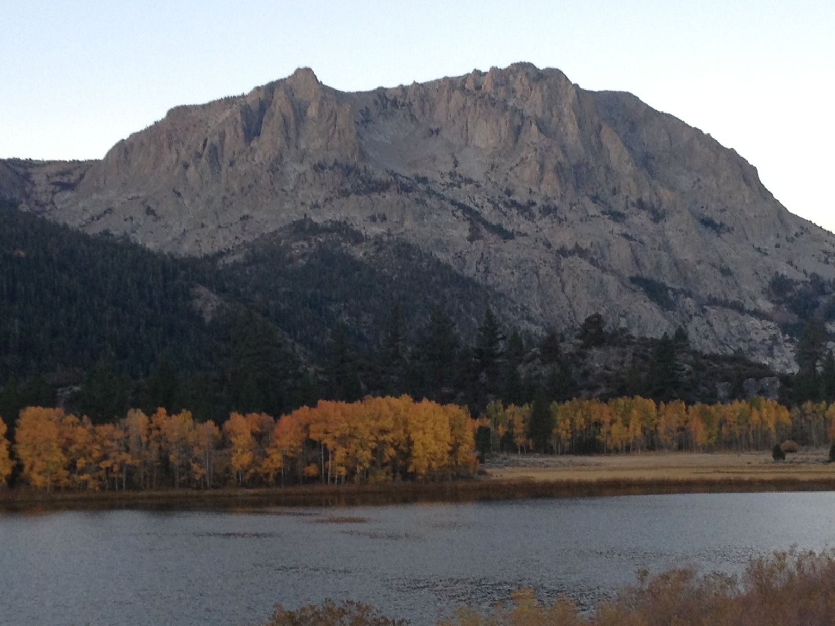 Un paysage montagneux avec un lac au premier plan et des arbres aux couleurs automnales.