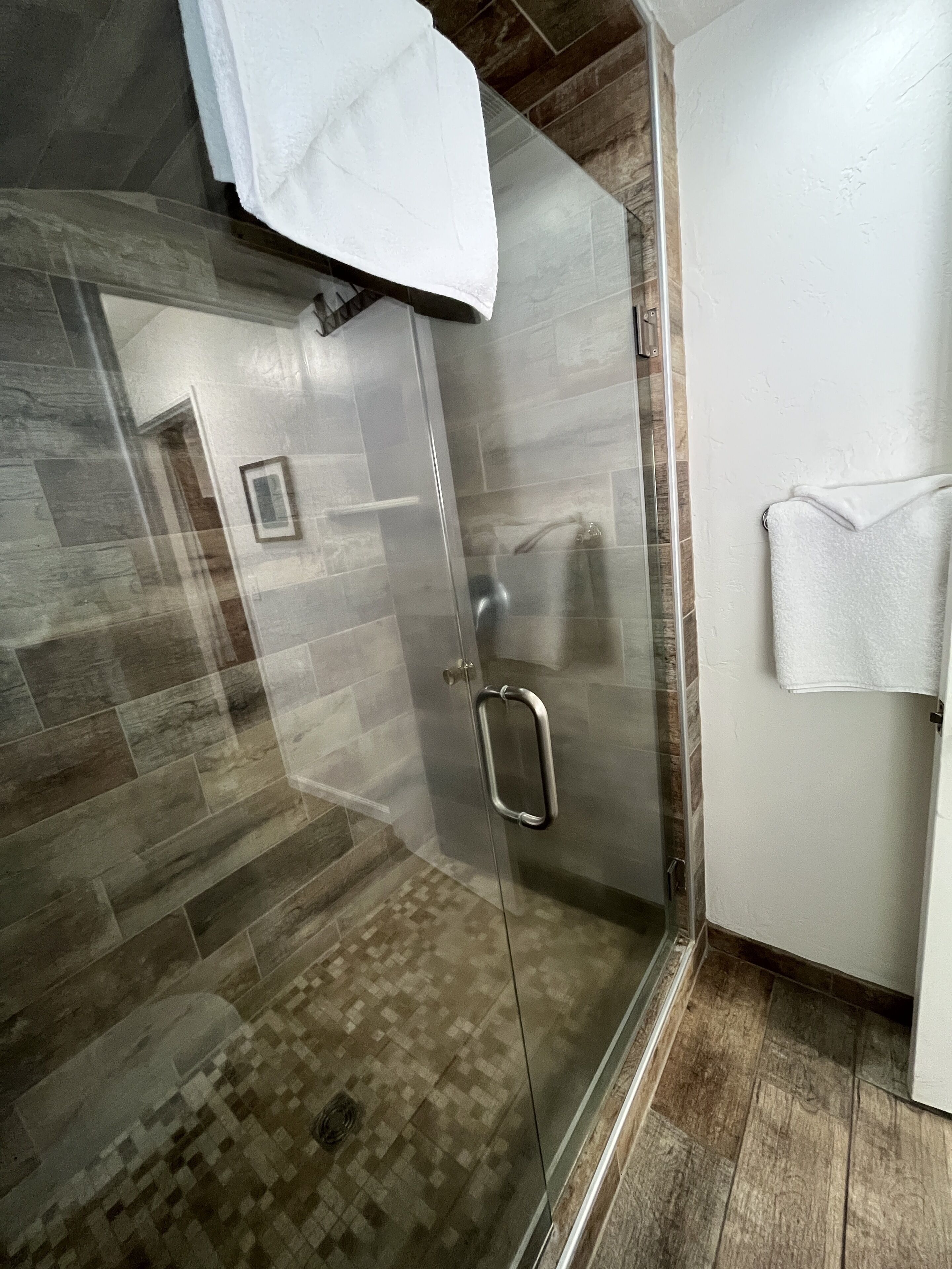 A modern bathroom with a glass shower enclosure, a white towel hanging on the wall, and a patterned floor.
