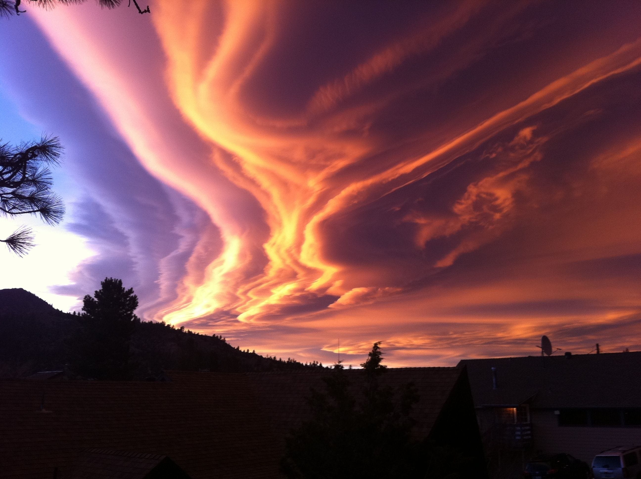 Un atardecer con nubes vibrantes de color naranja y morado sobre una zona residencial con casas y árboles.