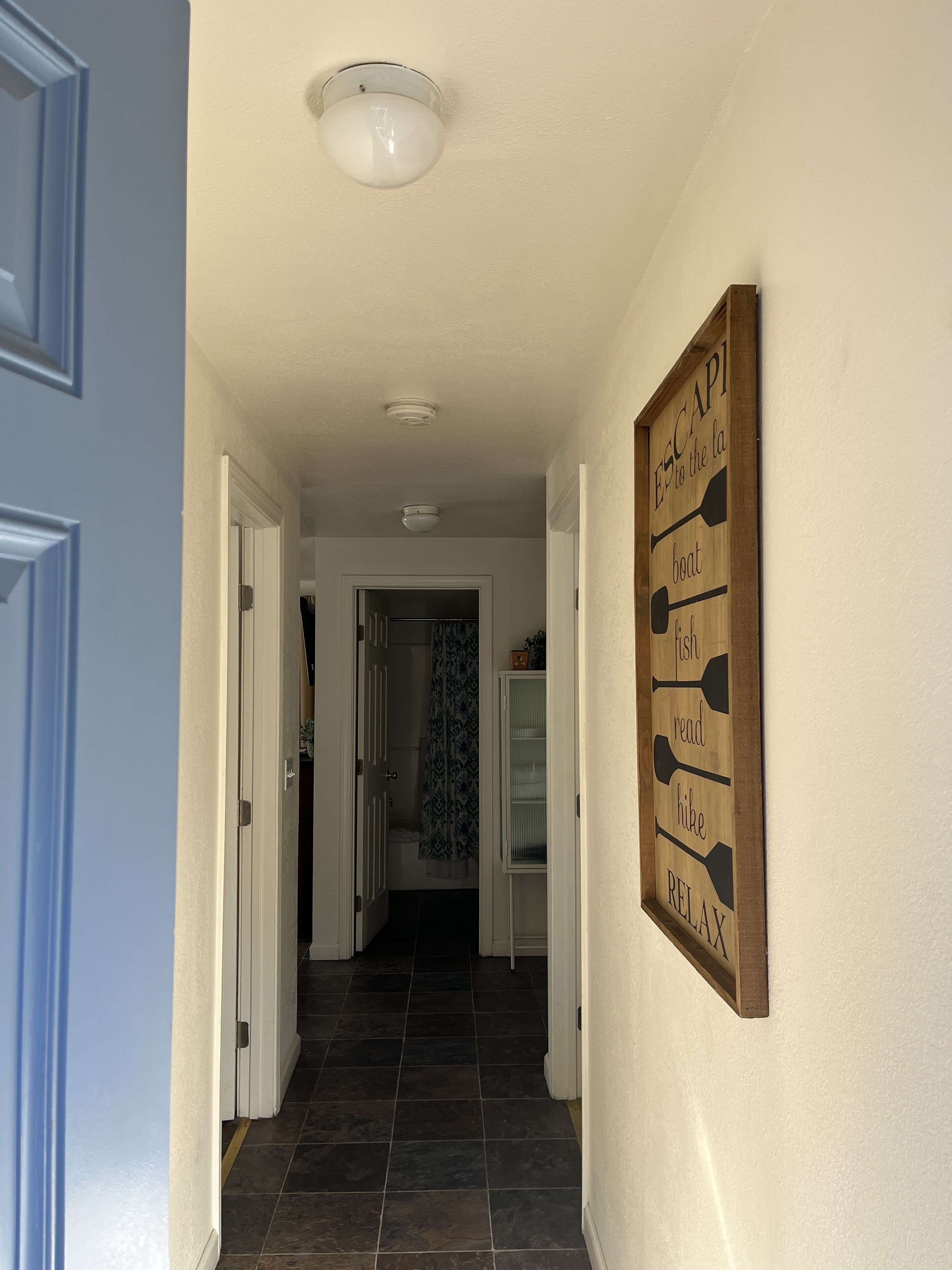 Ein Flur mit einem Holzschild an der Wand, einer Deckenleuchte und einer Tür zu einem Badezimmer.