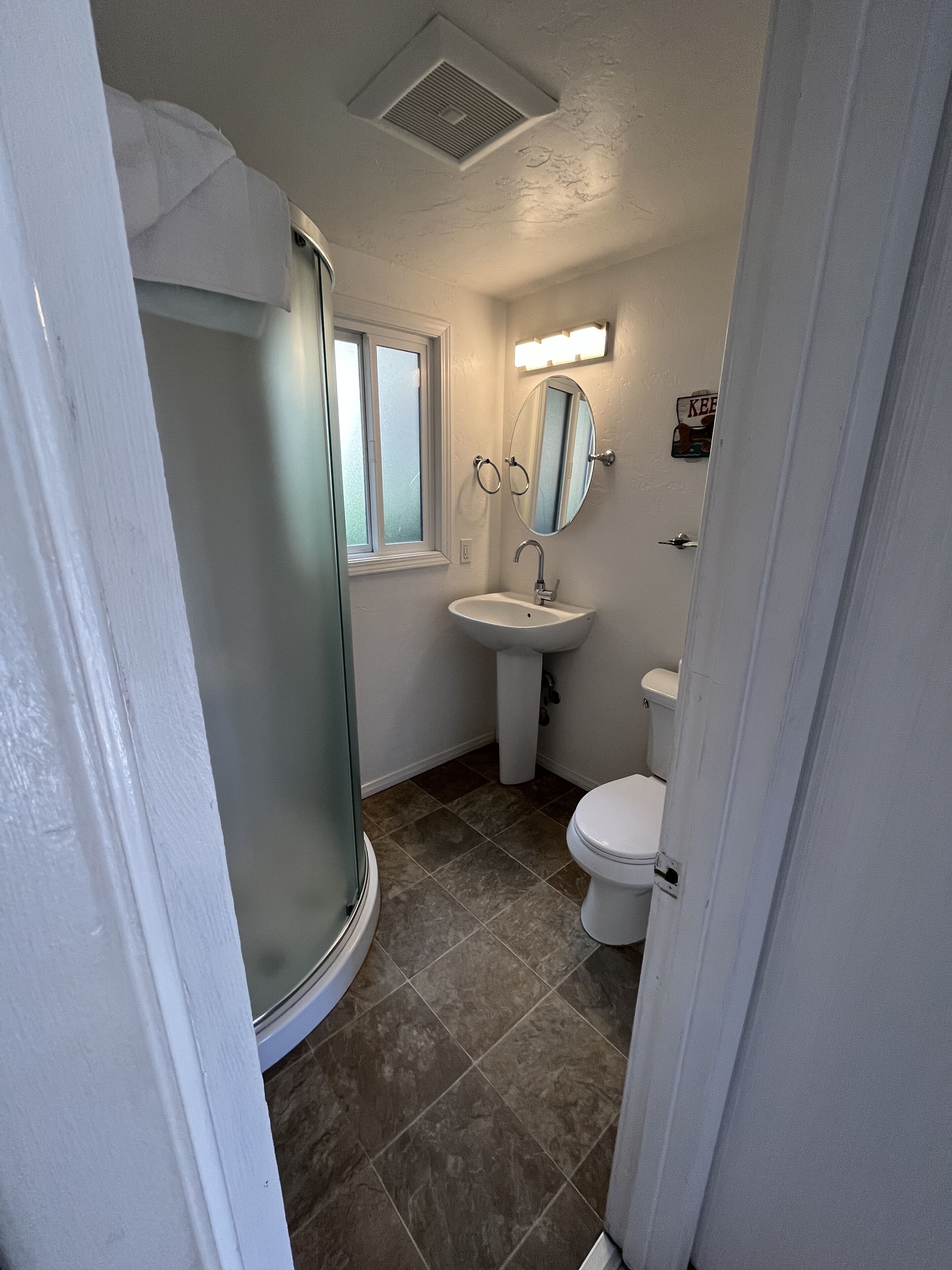 A bathroom with a shower, sink, toilet, and a window.