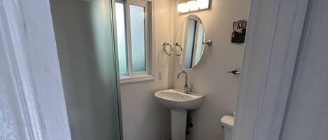 A bathroom with a shower, sink, toilet, and a window.