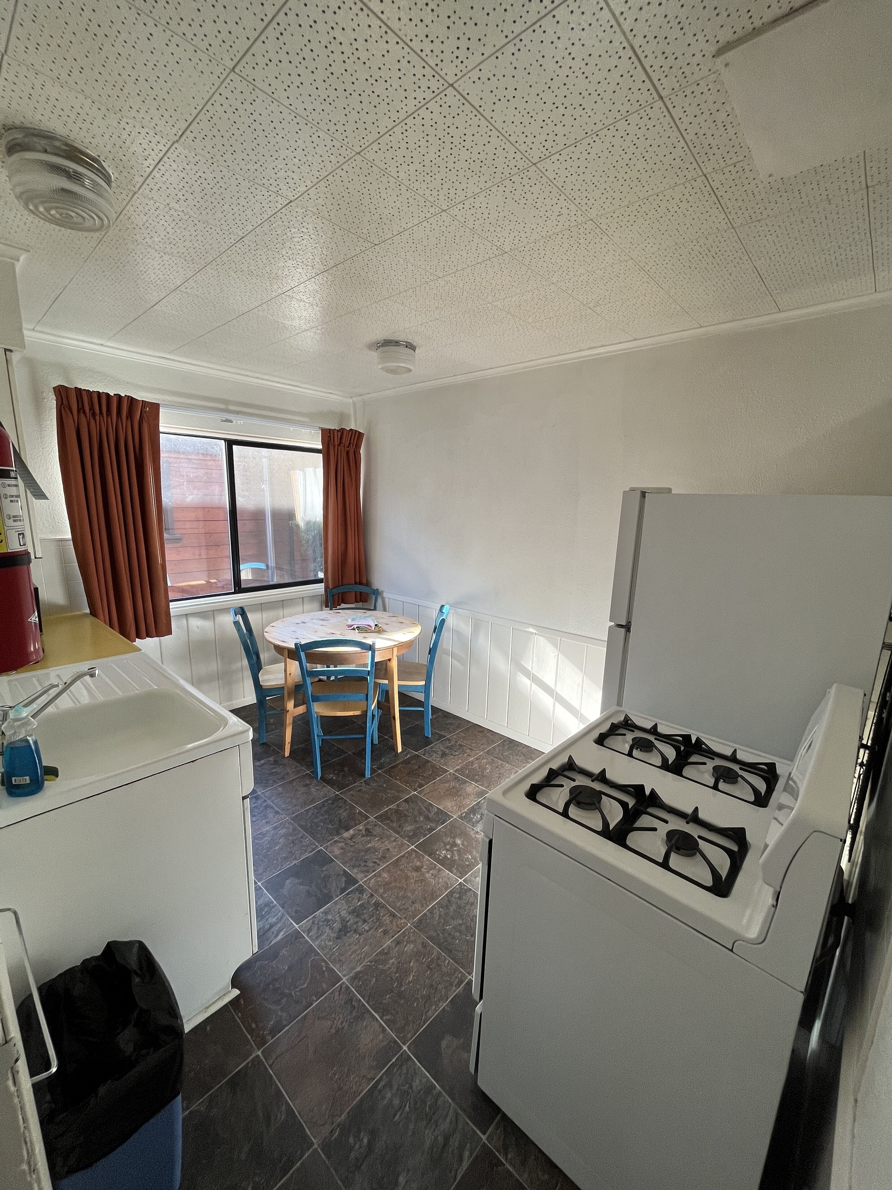 Cocina compacta con estufa a gas, un lavamanos y zona de comedor con mesa y sillas.