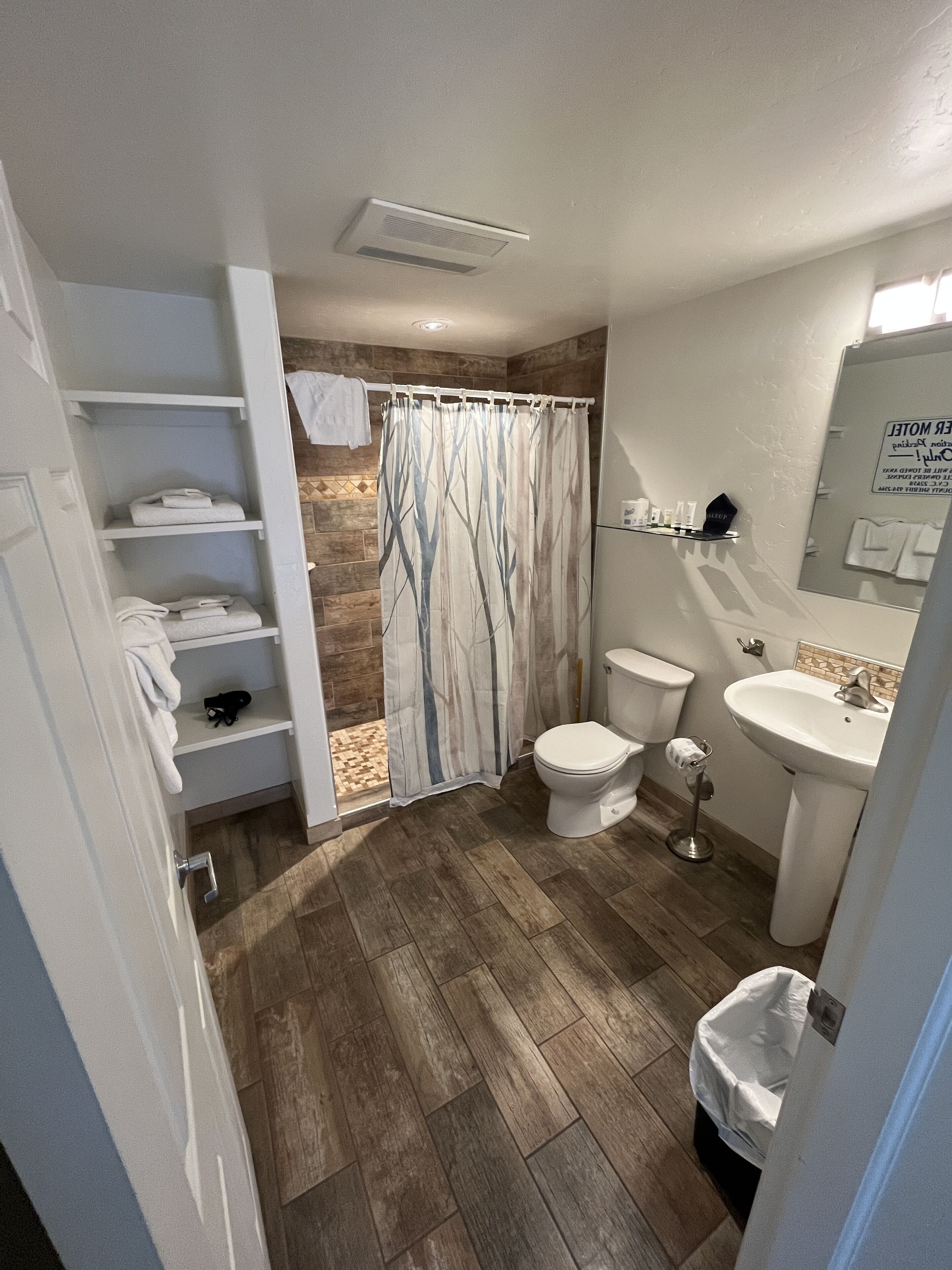 Et badeværelse med bruseforhæng, toilet, vask og hylder med håndklæder.