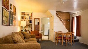 A cozy living room with a sofa, a dining table with chairs, a bookshelf, and a staircase leading to another room. - June Lake Villager (June Lake)