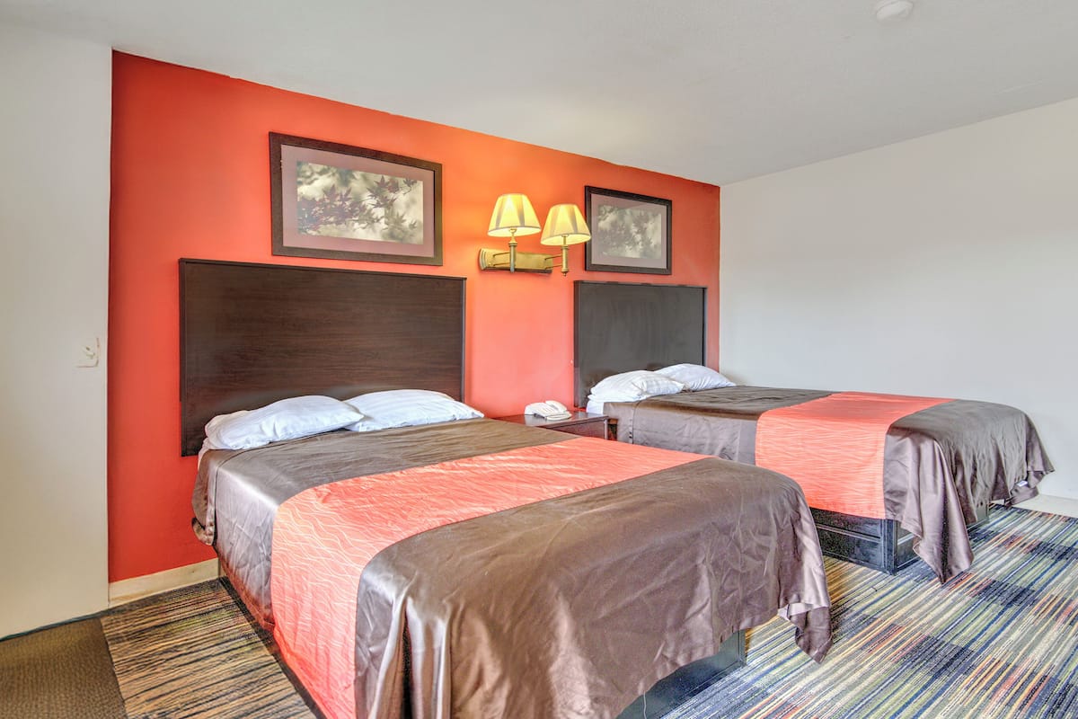 A hotel room with two beds, a red wall, and a striped carpet.