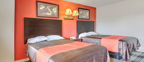 A hotel room with two beds, a red wall, and a striped carpet.