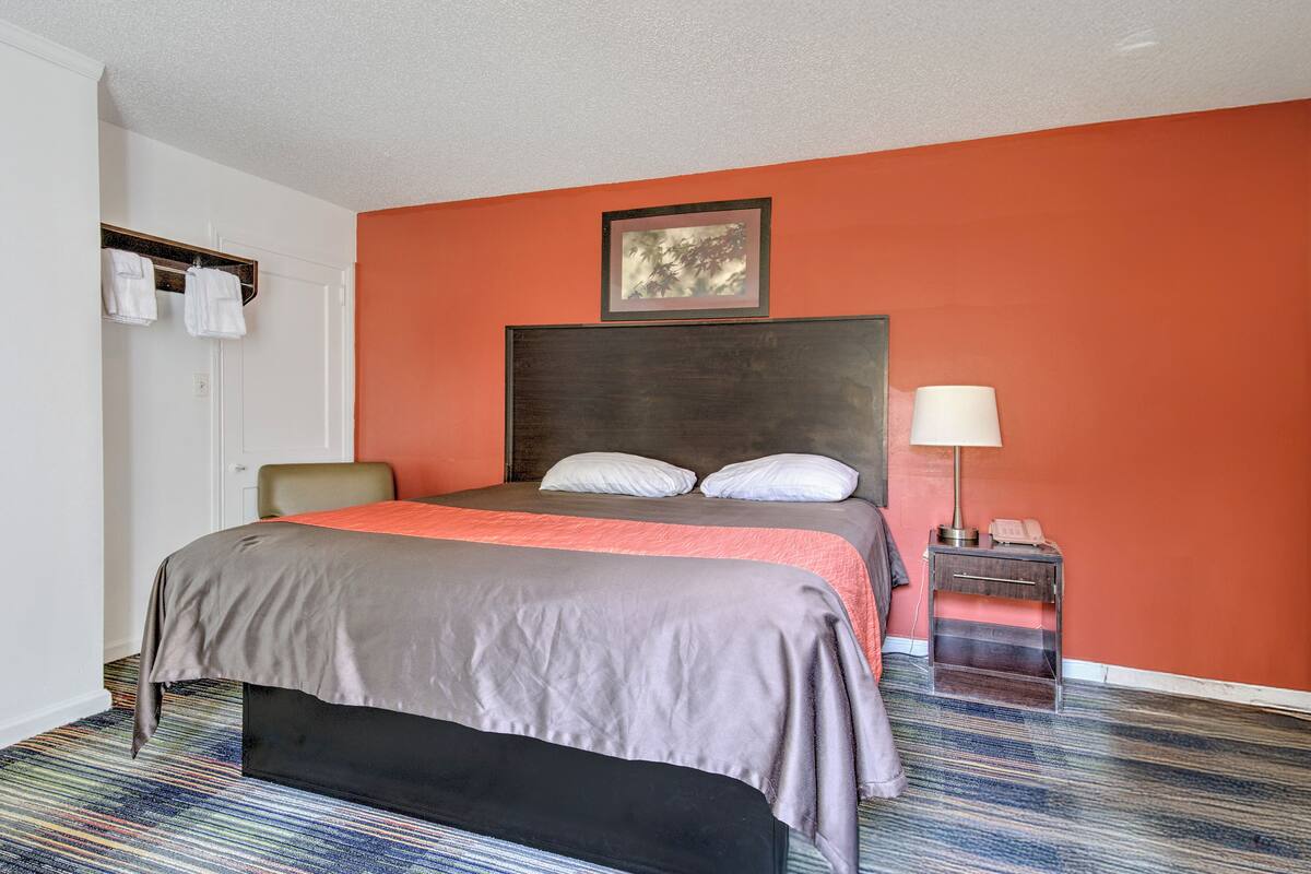 A hotel room with a bed, a chair, a bedside table with a lamp, and a framed picture on the wall.