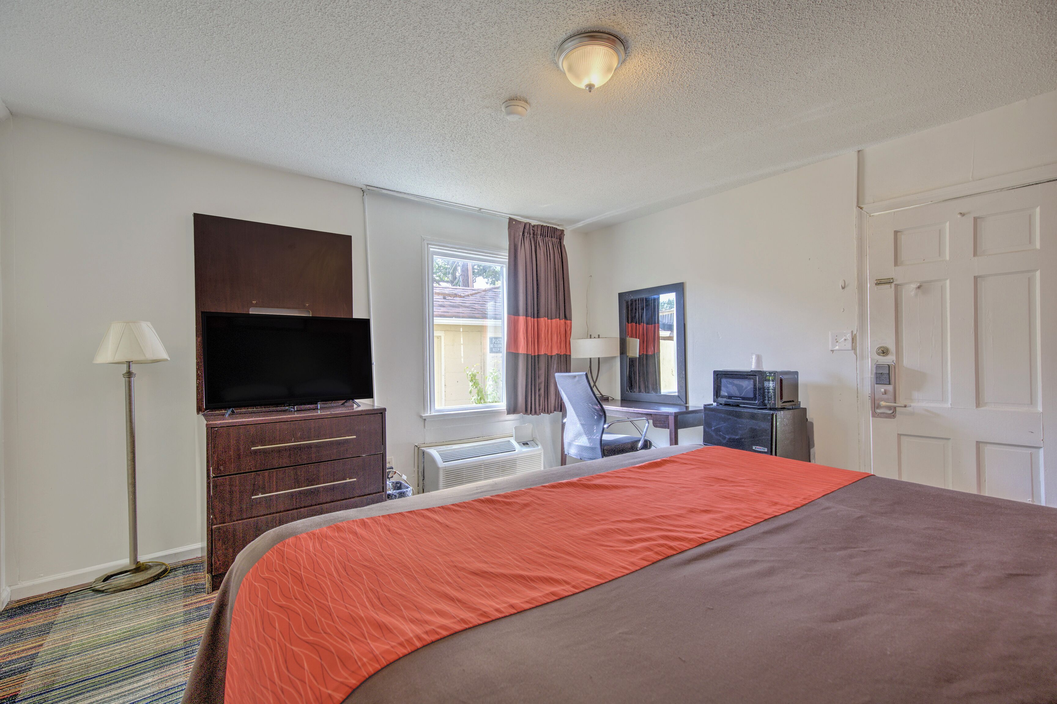 A hotel room with a bed, a desk with a computer, a television, and a window with curtains.