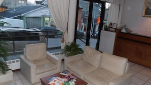 Un salon avec un canapé et des fauteuils, une table basse avec des magazines, et une vue sur la rue.