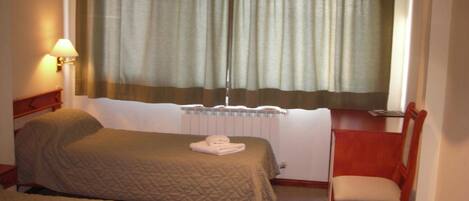 Habitación de hotel con dos camas, una silla, un escritorio, una lámpara y un ventanal con cortinas.
