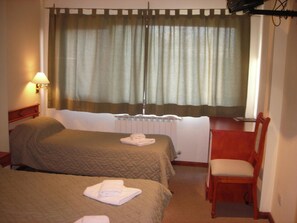 Ein Hotelzimmer mit zwei Betten, einem Sessel, einem Schreibtisch, einer Lampe und einem Fenster mit Vorhängen.