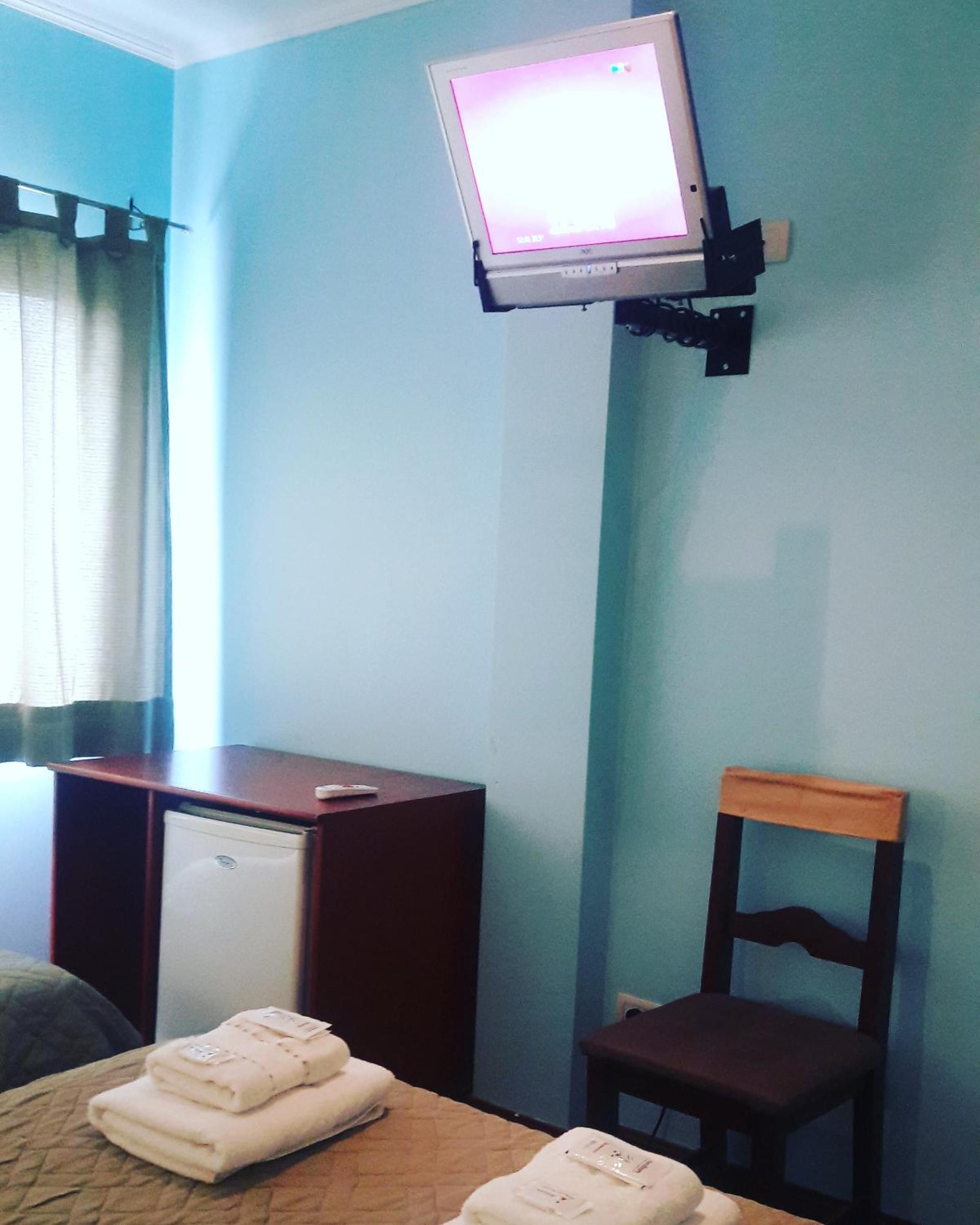 A hotel room with a bed, a desk, a chair, and a television mounted on the wall.