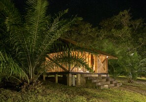 A wooden structure with a staircase leading up to a door, surrounded by lush greenery.