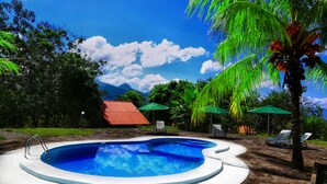 A swimming pool with a stone deck, surrounded by palm trees and a red-roofed building. - Huasai Wasi Ecolodge (San Antonio de Cumbaza)
