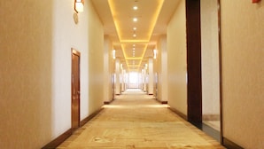 Een lange, smalle hotelgang met een tapijtvloer, houten deuren en inbouwverlichting.