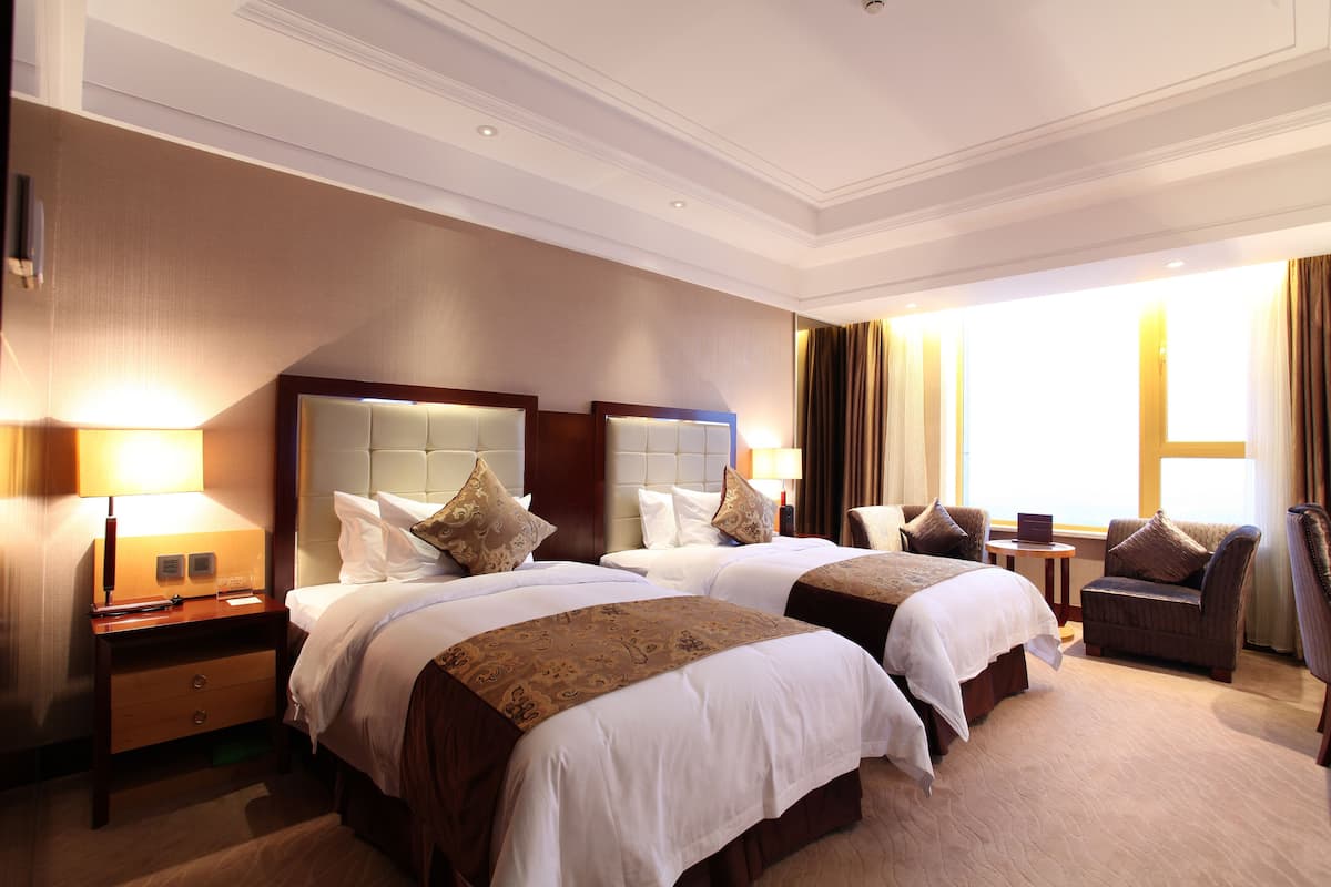 A hotel room with two beds, a sitting area, and a large window.