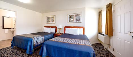 A hotel room with two beds, a bathroom, and a window with curtains.