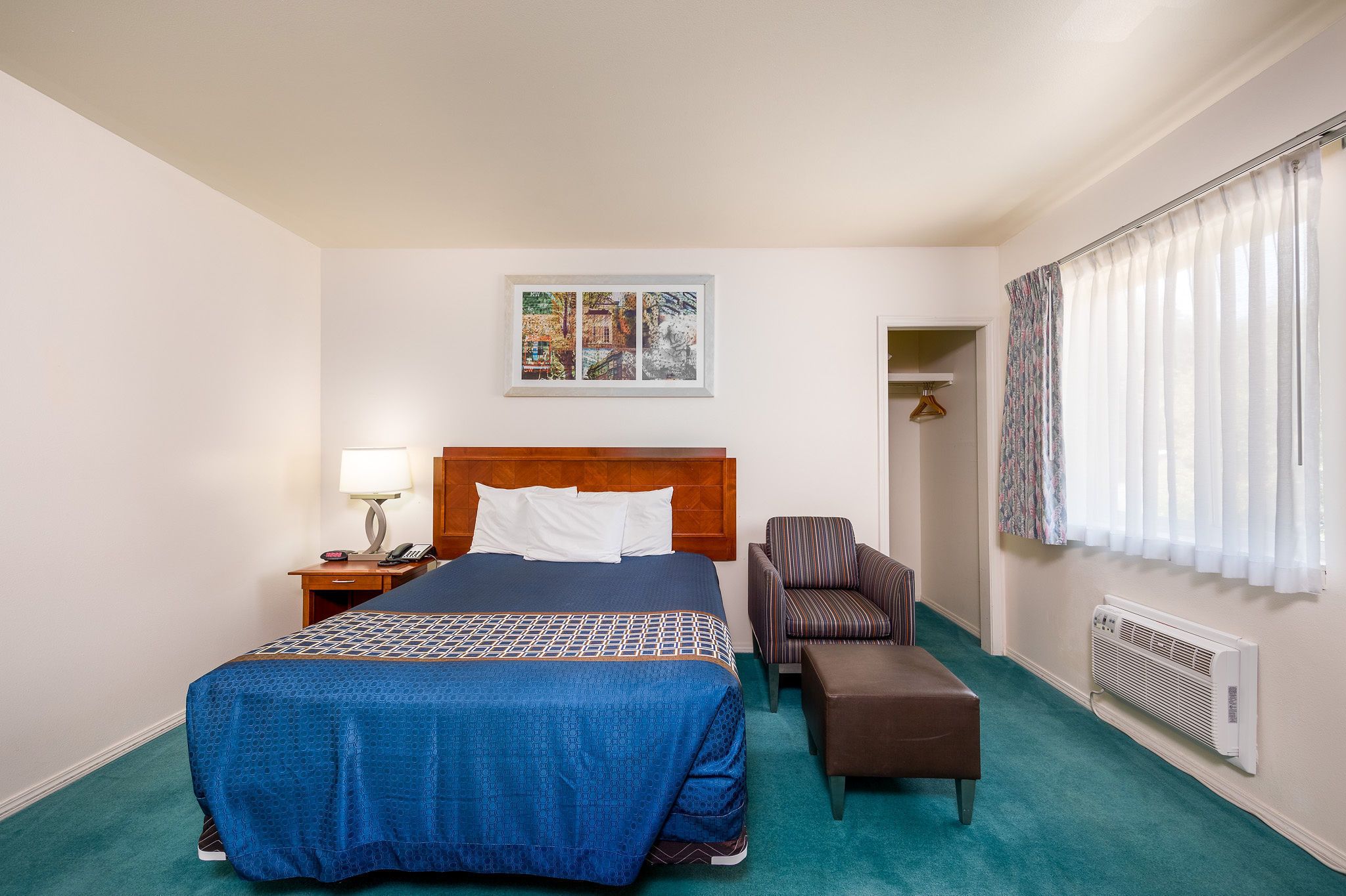 A hotel room with a large bed, a chair, a small table, a lamp, a picture on the wall, and a window with curtains.