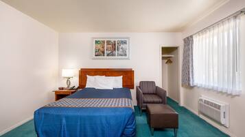 A hotel room with a large bed, a chair, a small table, a lamp, a picture on the wall, and a window with curtains.