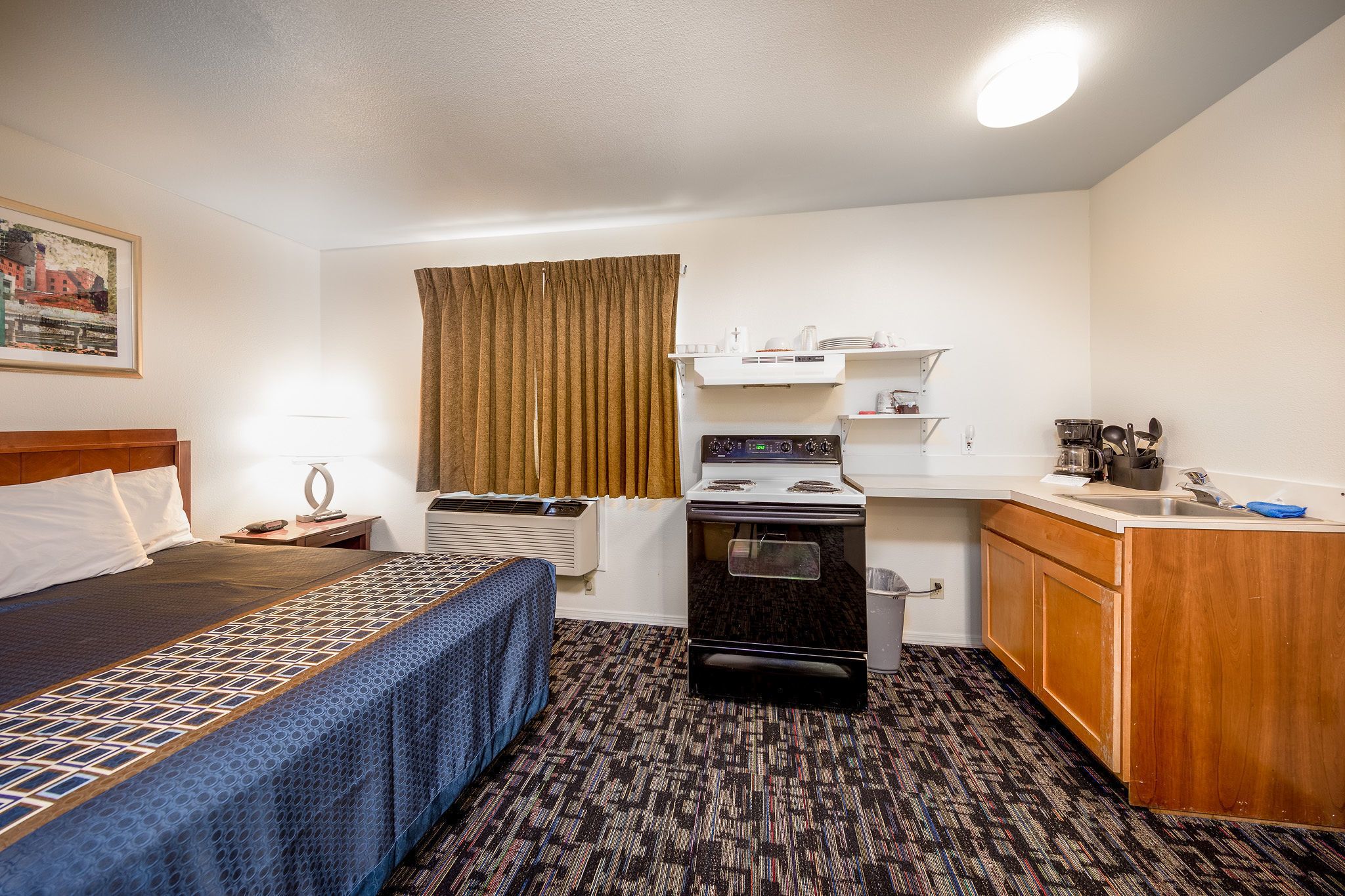 Habitación de hotel compacta con cama, kitchenette, estufa y una pequeña encimera.
