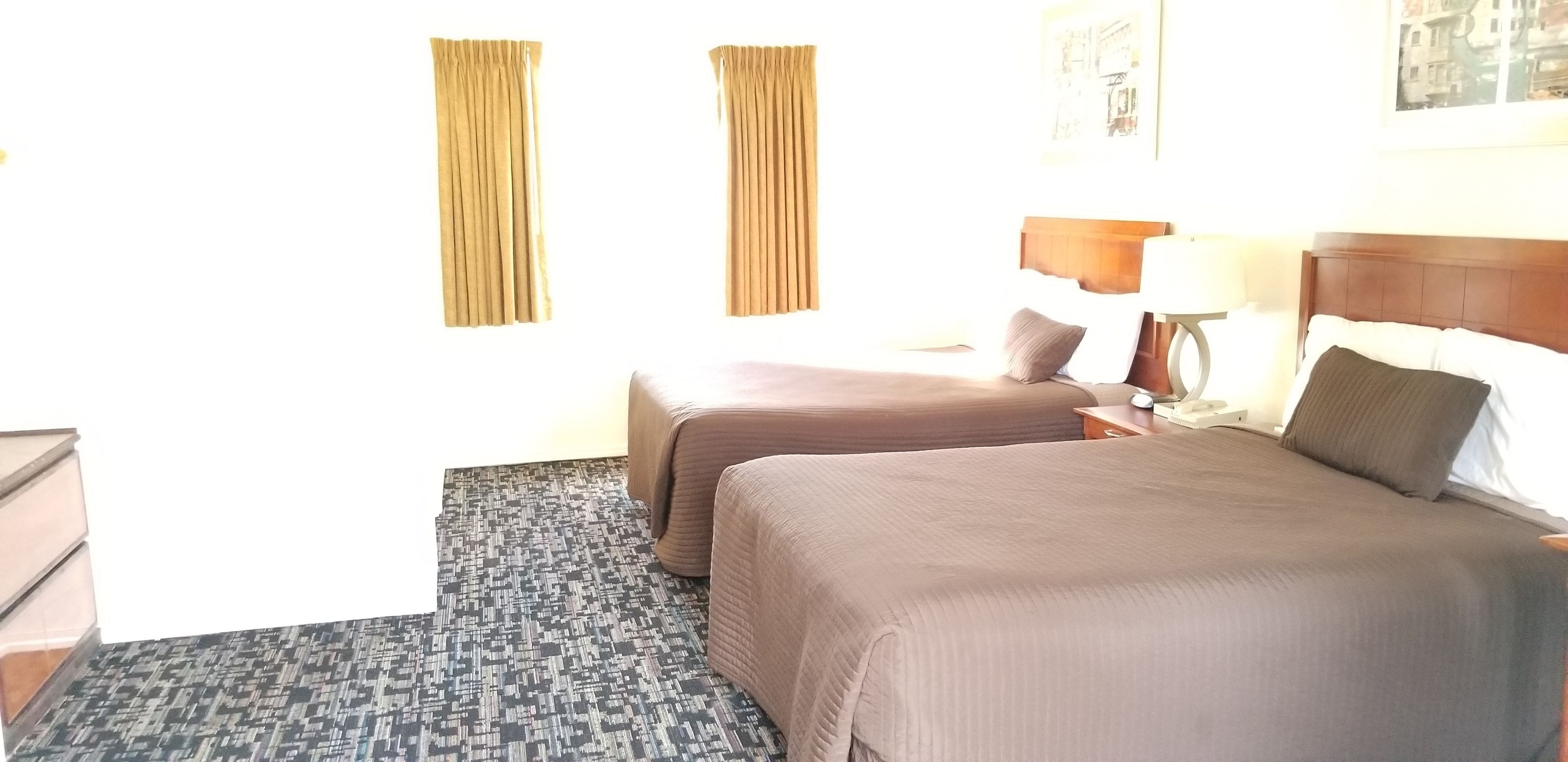 Ein Hotelzimmer mit zwei Betten, einem gemusterten Teppich, einem Holz-Kopfteil und einem Nachttisch mit Lampe.
