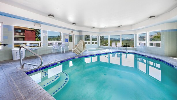 A swimming pool with clear blue water, a sun terrace with chairs, and a view of a mountain.