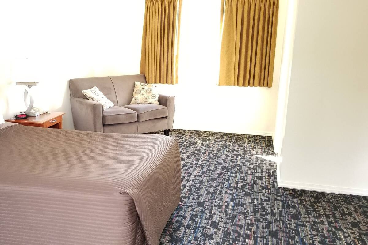 A hotel room with a bed, a chair, a nightstand, and a patterned carpet.