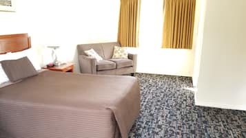 A hotel room with a bed, a chair, a nightstand, and a patterned carpet.