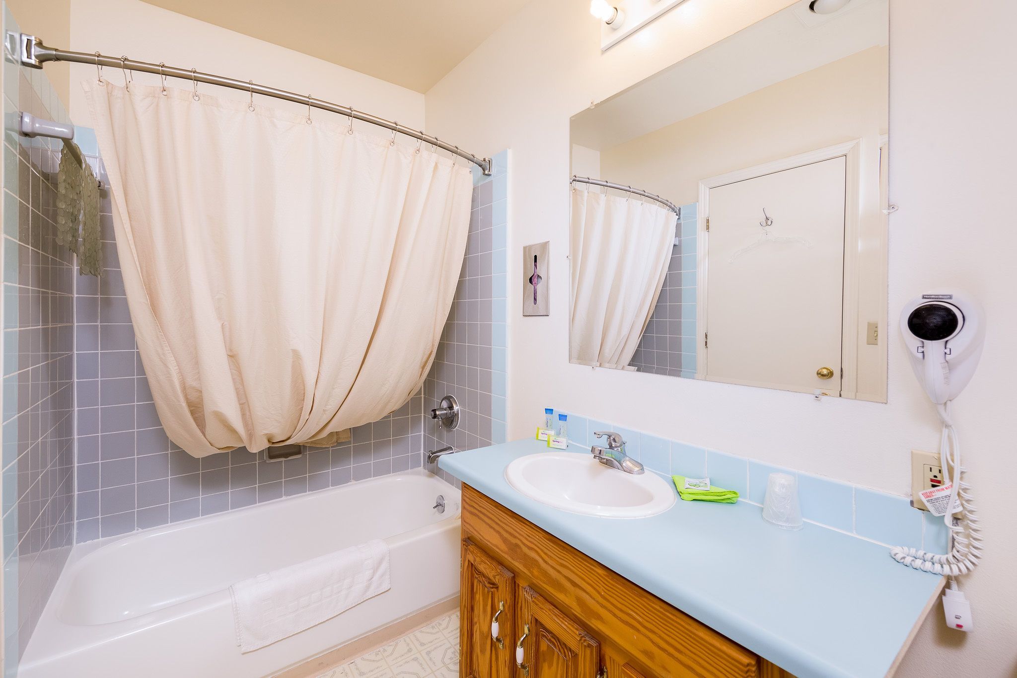 A bathroom with a bathtub, a sink, a mirror, and a hairdryer.