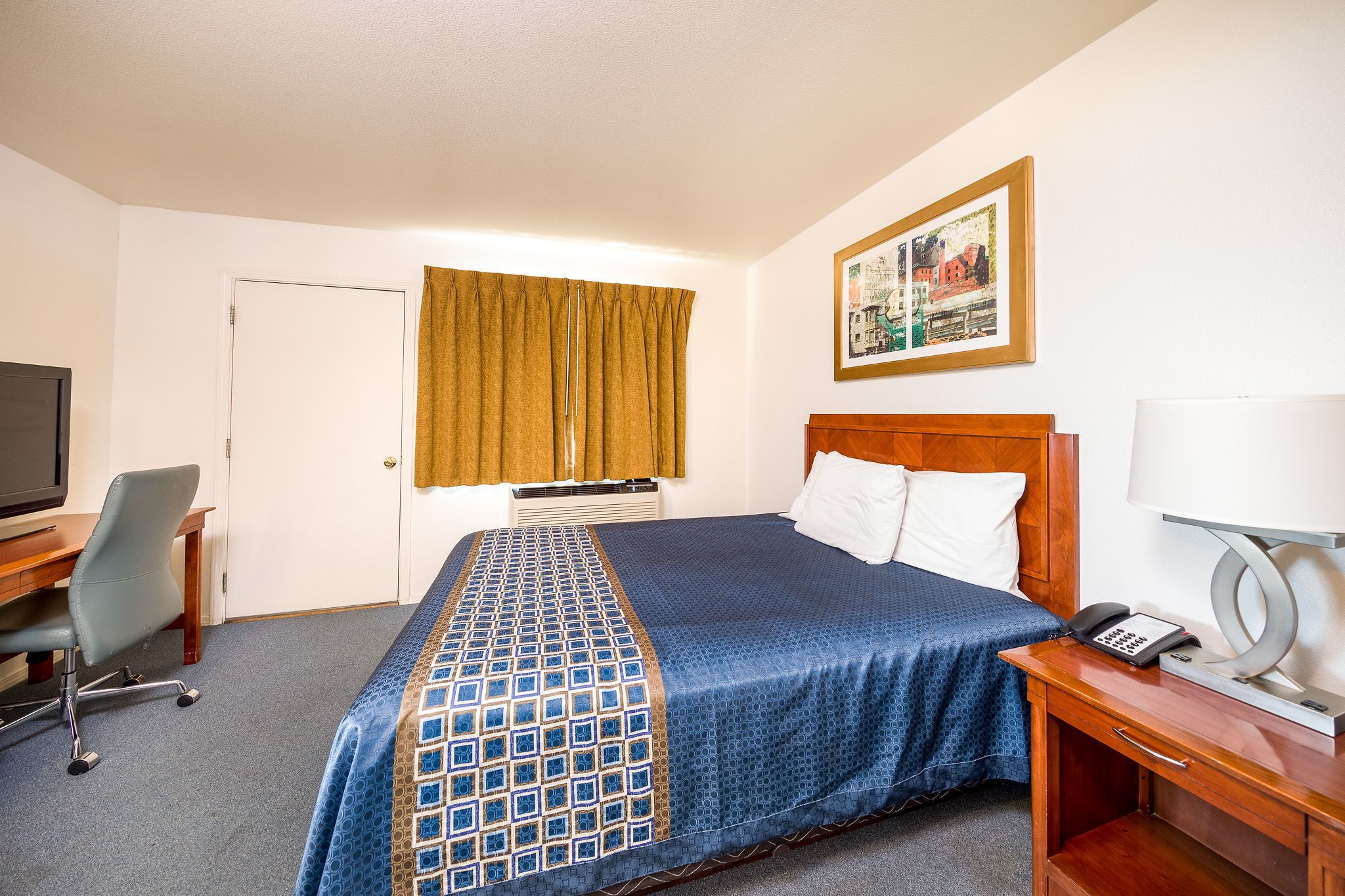 A hotel room with a bed, a desk with a chair, a television, a telephone, and a painting on the wall.