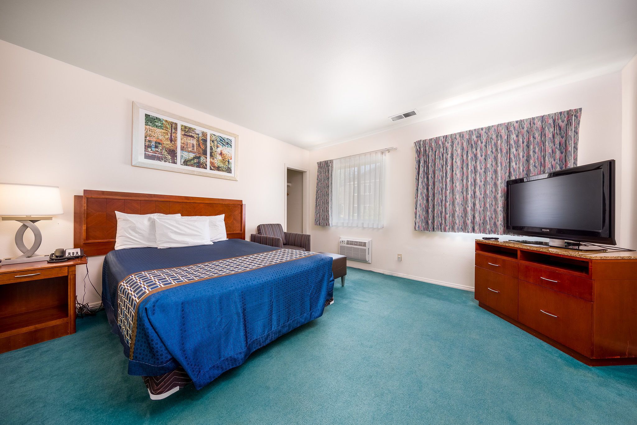 A hotel room with a bed, a TV, a desk, and a window with curtains.