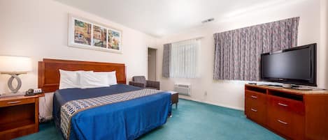 A hotel room with a bed, a TV, a desk, and a window with curtains.