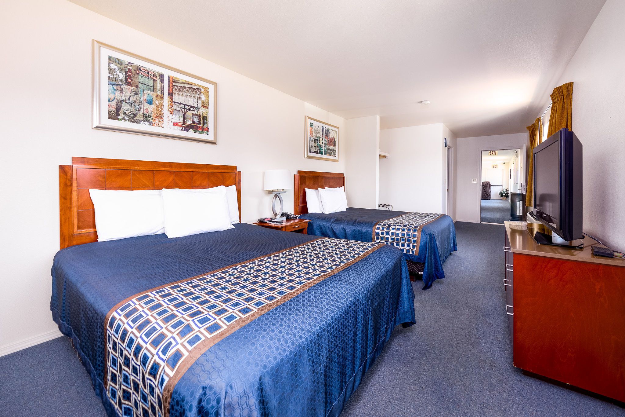 A hotel room with two beds, a TV, a desk, and artwork on the walls.