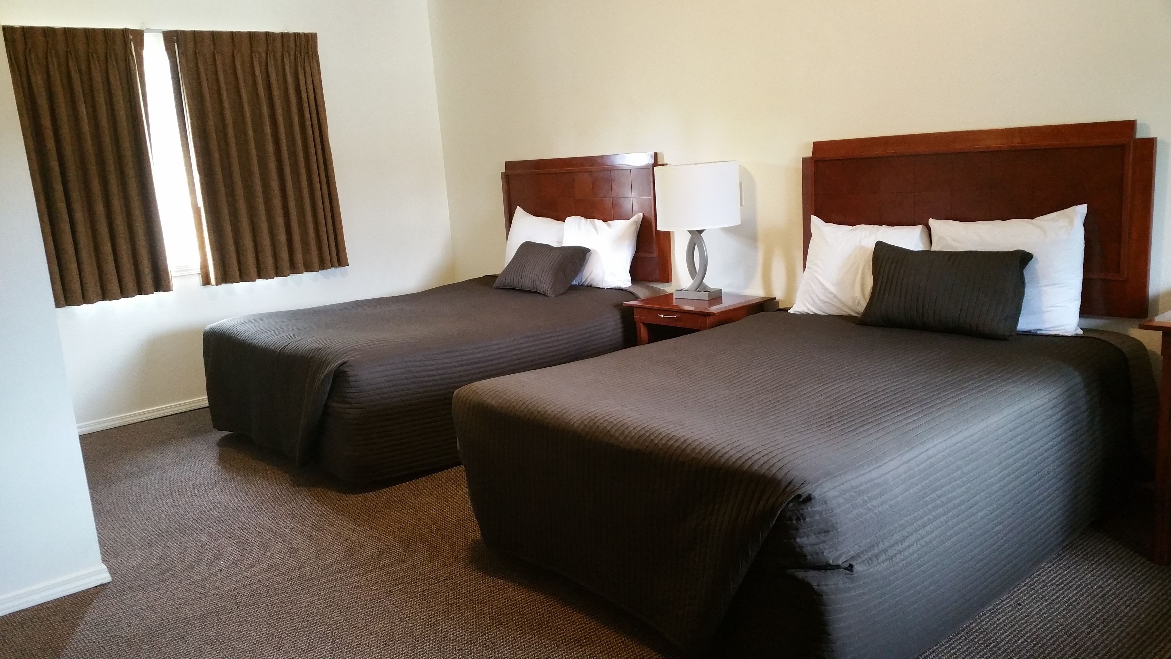 A hotel room with two beds, a nightstand with a lamp, and a window with curtains.