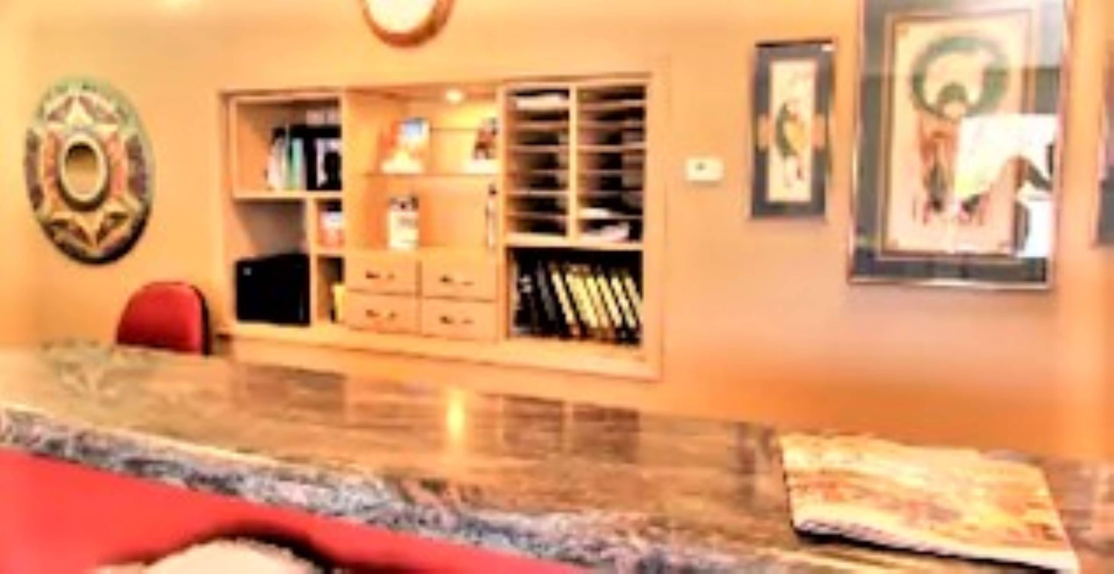 A room with a marble countertop, a red chair, a bookshelf, and a framed picture on the wall.