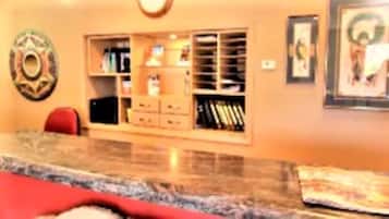 A room with a marble countertop, a red chair, a bookshelf, and a framed picture on the wall.