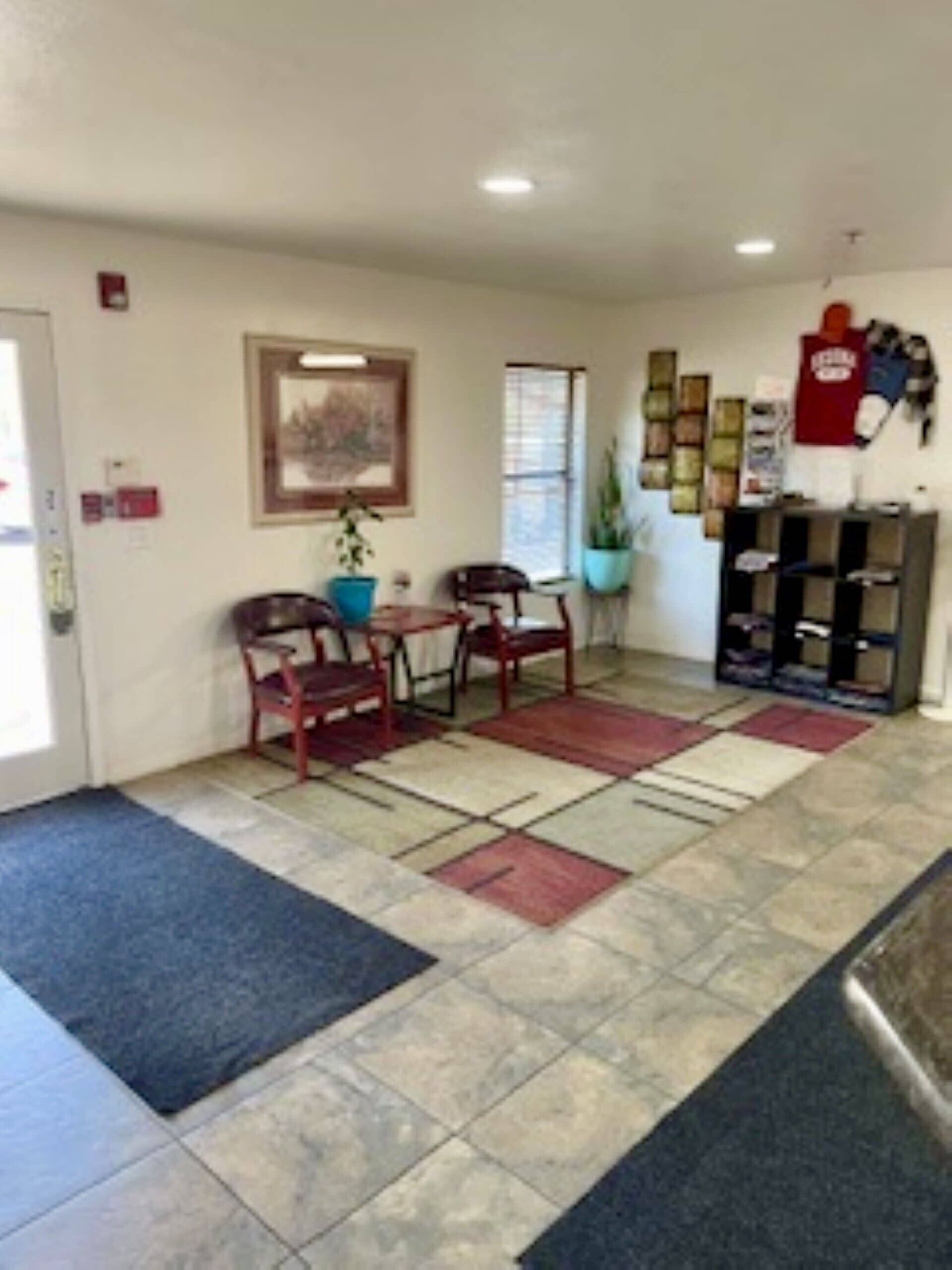 A reception area with a tiled floor, a reception desk, a framed picture on the wall, and a potted plant.