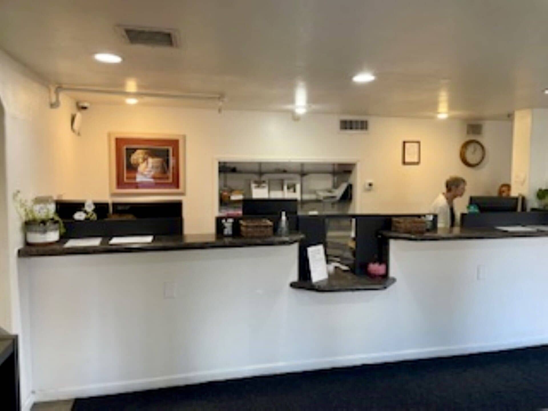 A reception desk with a computer, a framed picture on the wall, and a clock.