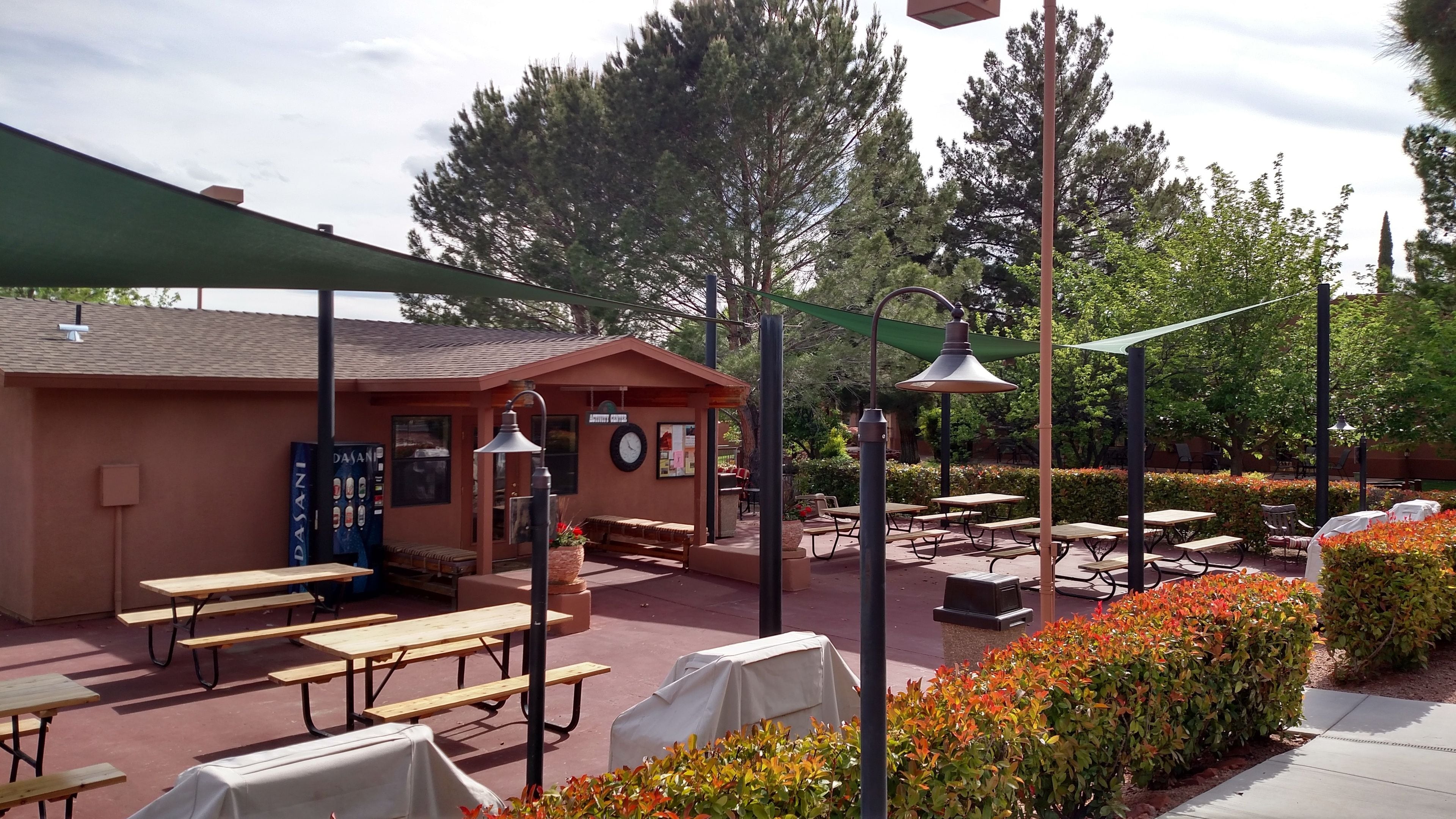Un patio al aire libre con mesas de picnic, asientos cubiertos y un edificio con un reloj y un letrero.