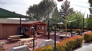 An outdoor patio area with picnic tables, covered seating, and a building with a clock and a sign.