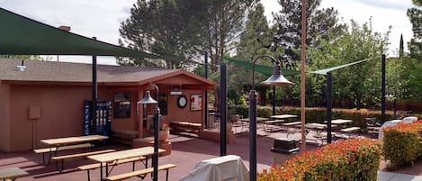 Un patio al aire libre con mesas de picnic, asientos cubiertos y un edificio con un reloj y un letrero.