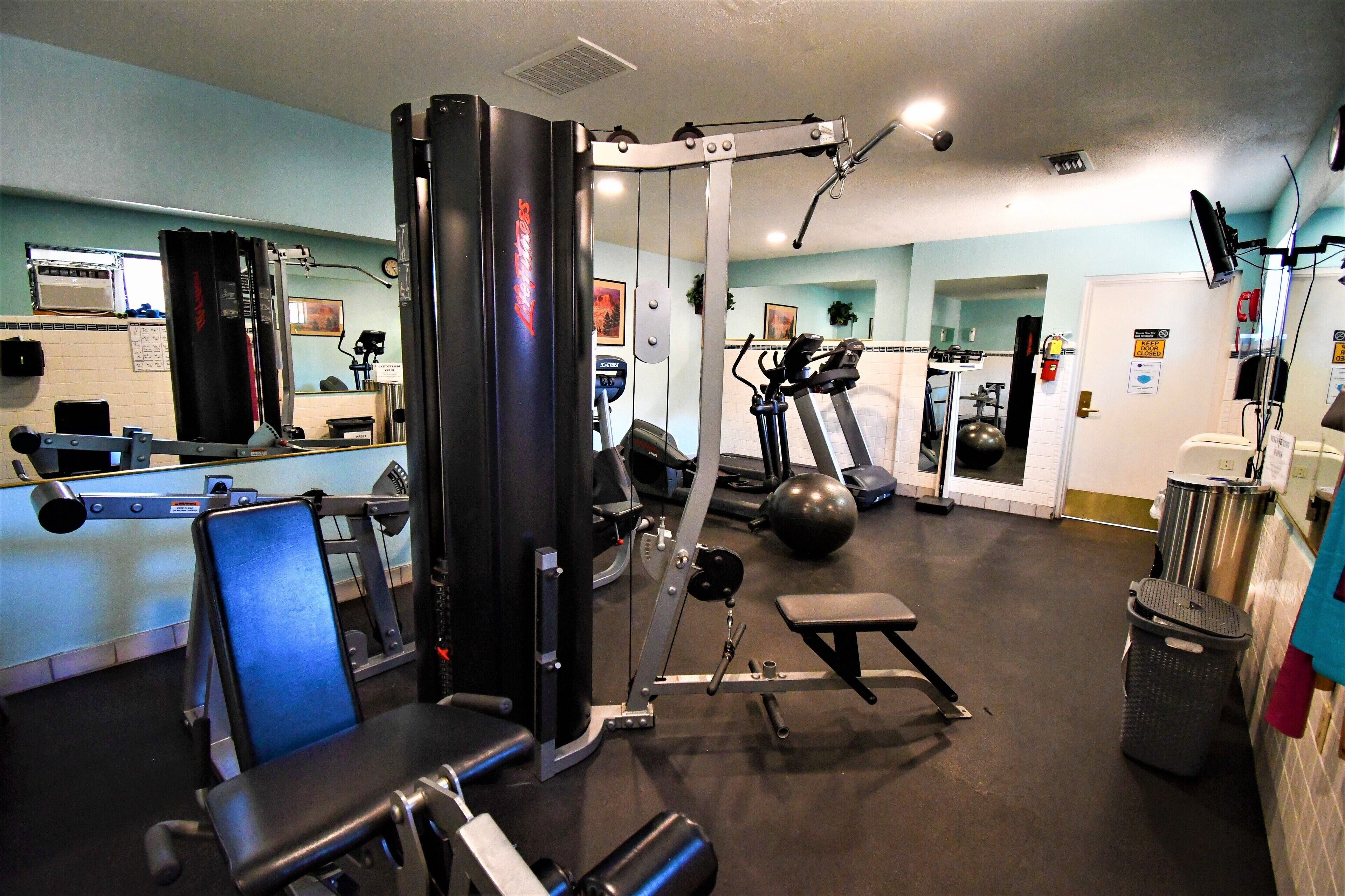 Ett gym med träningsredskap, en spegel och en papperskorg.