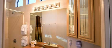 A bathroom with a sink, mirror, vanity, towel rack, shower, and a hairdryer.
