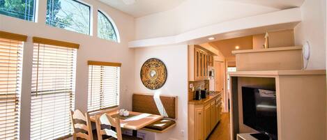 A compact kitchen with a built-in TV, wooden cabinets, and a dining area with a bench and chairs.