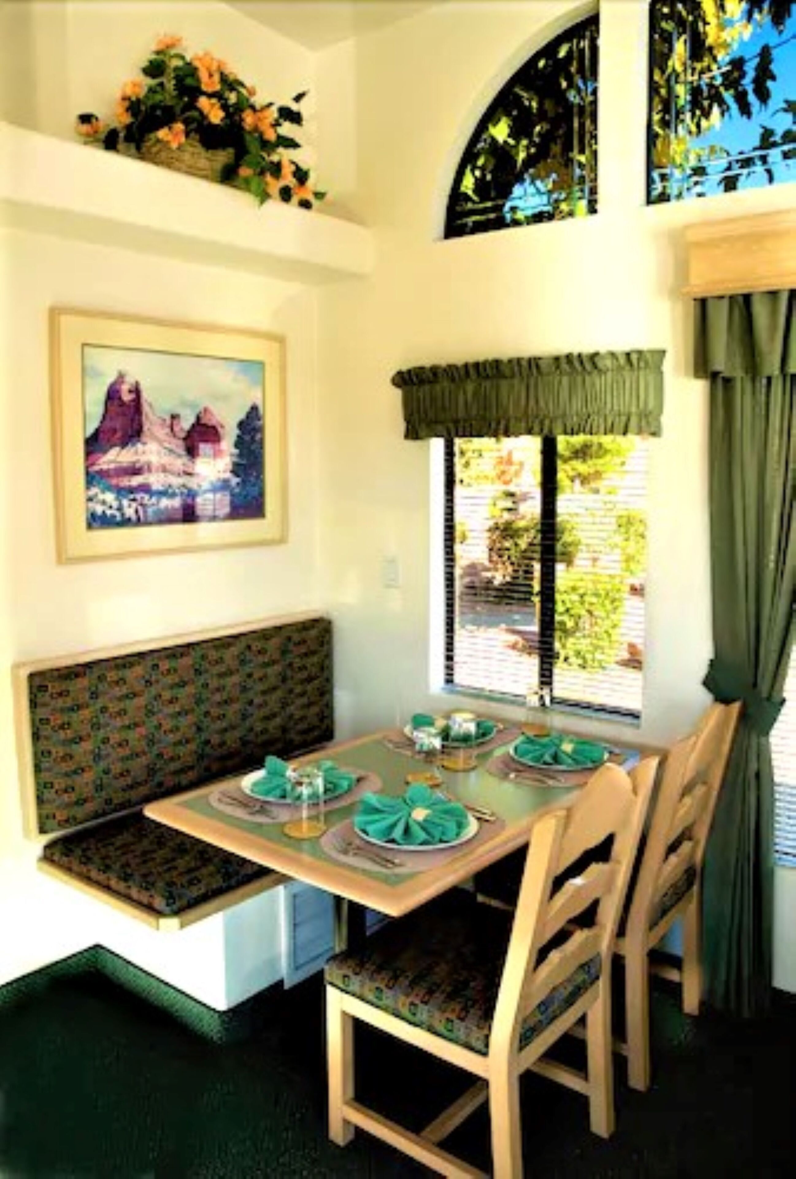 A dining area with a table set for four, a bench, and a window with curtains.