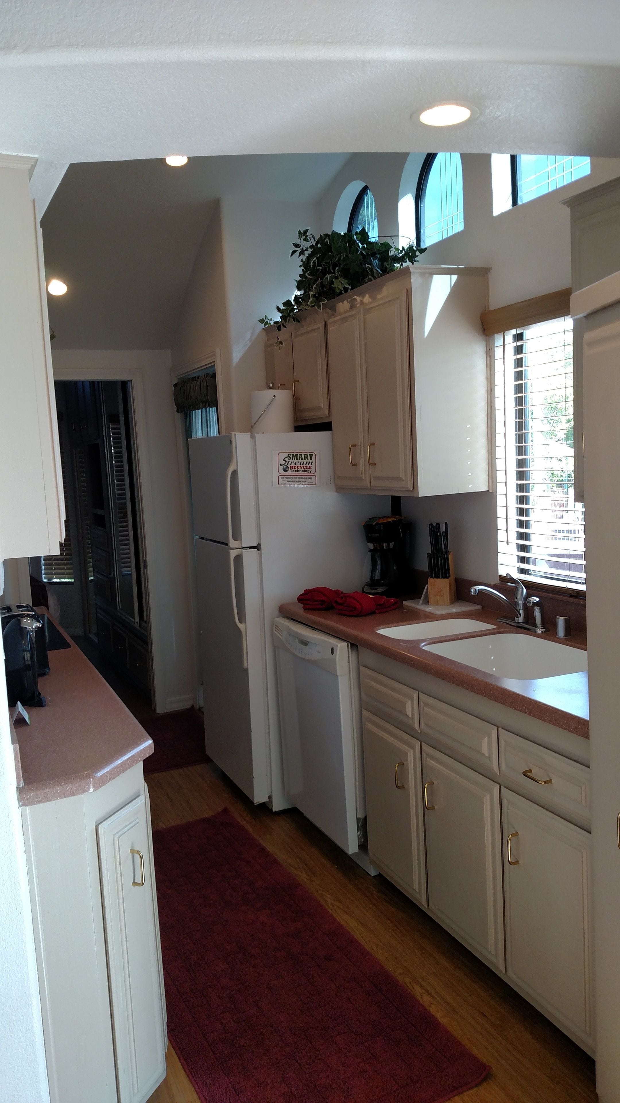 A kitchen with white cabinets, a red rug, a coffee maker, and a sign about smart refrigeration technology.