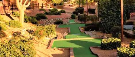 En miniatyrgolfbana med en grön yta för att putta på, omgiven av vackert anlagda områden och träd.