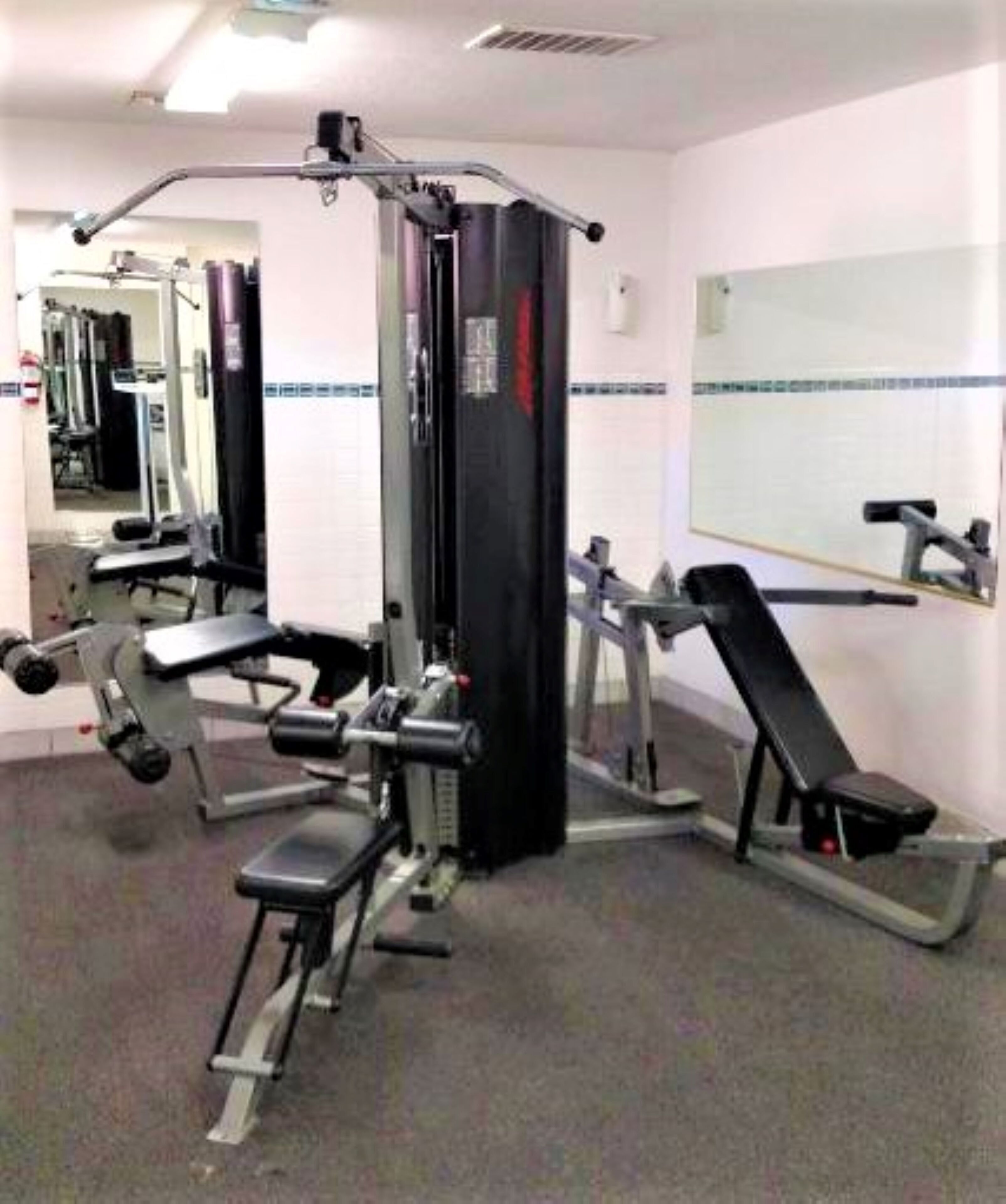 A gym with various exercise equipment including a bench press, a squat rack, and a cable machine.